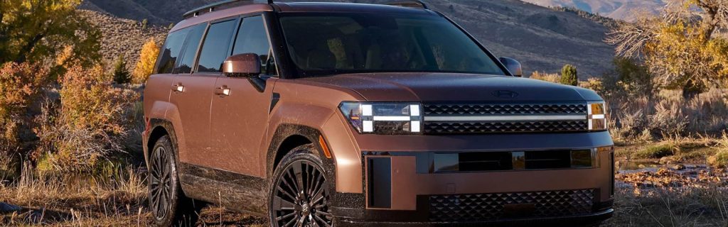 Front view of a brown SUV parked in a rugged, natural landscape with autumn foliage.